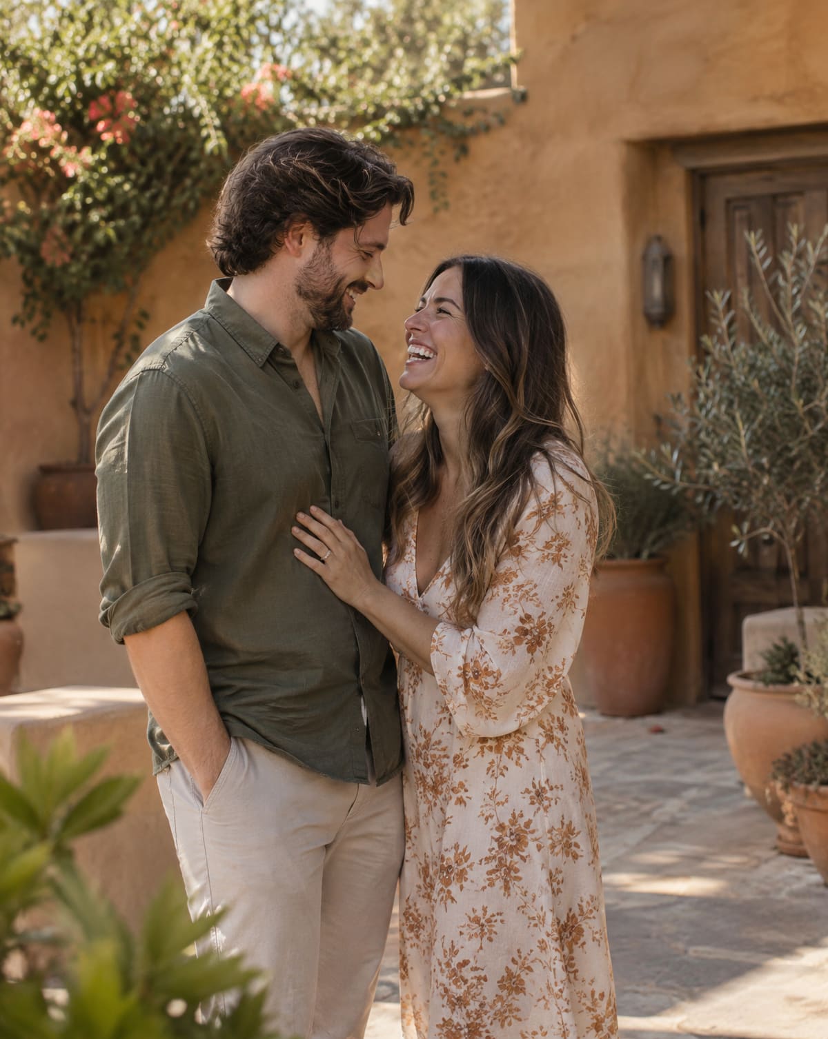 A couple laughs together in a sunlit adobe courtyard during a portrait session, clay walls glowing behind them